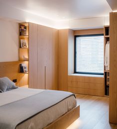 a bed room with a neatly made bed and wooden shelves next to a large window