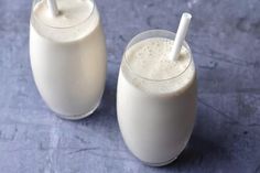 two glasses filled with milk sitting next to each other on top of a blue table