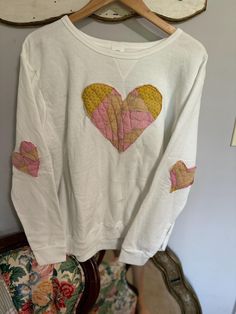 a white shirt with pink and yellow hearts on it hanging from a wooden hanger