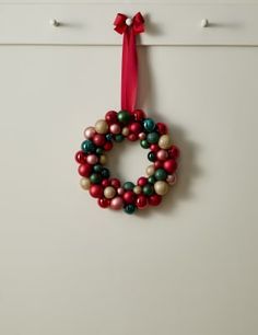 a christmas ornament hanging on the wall with a red ribbon and green balls