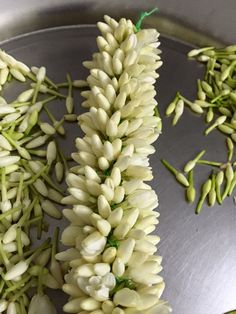 some white flowers sitting on top of a metal tray next to green stems and buds