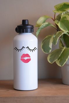 a white water bottle with pink lips and eyelashes on it next to a potted plant