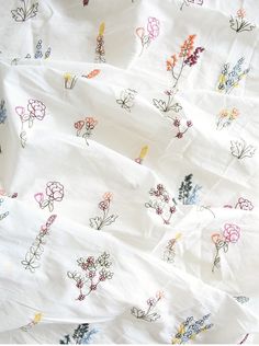 an unmade bed covered in white sheets with colorful flowers on them