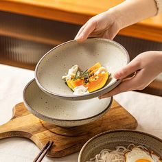 a person holding a bowl with food in it on top of a wooden tray next to other bowls