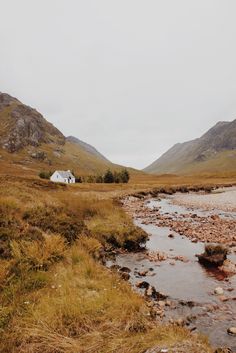 a small white house sitting on top of a lush green hillside next to a river