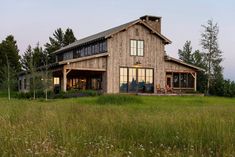 a large wooden house sitting in the middle of a lush green field with tall grass