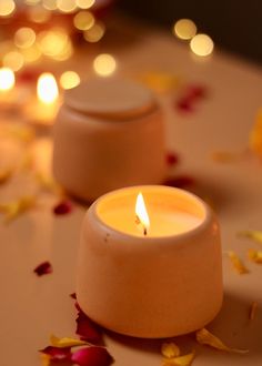 two white candles sitting on top of a table covered in petals and petals around them