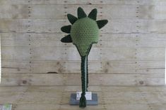 a crocheted green flower head on a stand in front of a wooden wall