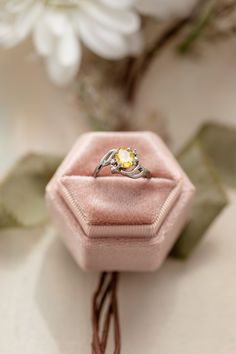 an engagement ring in a pink velvet box on a table with flowers and greenery