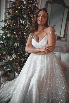 a woman in a wedding dress standing next to a christmas tree with her arms crossed