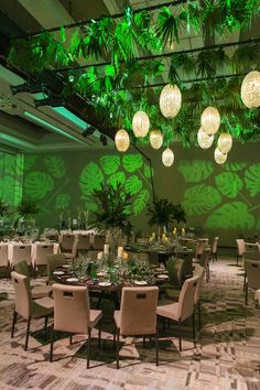 a large room with tables, chairs and plants on the walls is lit by hanging lights