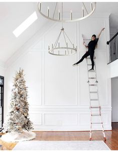 a woman climbing up the side of a ladder next to a christmas tree in a white room