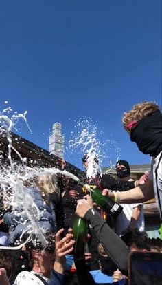 a group of people are splashing water on each other and holding bottles in the air