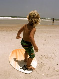 a little boy standing on top of a surfboard in the sand at the beach