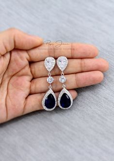 a hand holding three pairs of blue and white diamond drop earrings in their left hand