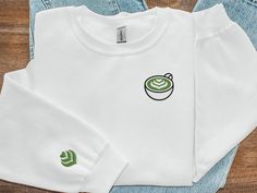 This Matcha embroidered crewneck sweatshirt is the perfect blend of style and comfort! Whether you're out and about or cuddled up at home, our crewnecks feature minimalistic designs that can be paired with any outfit. The surprise sleeve design perfectly complements the front, offering a whimsical touch that will make you smile throughout the day! Product Details:  * 50% cotton, 50% polyester * Pre-shrunk * Classic fit * 1x1 athletic rib knit collar with spandex * Air-jet spun yarn with a soft f Matcha Mug, Matcha Lover, Embroidery Sweater, Tea Shirt, Art Embroidery, Embroidered Crewneck, Matcha Tea, Latte Art, Iron Decor