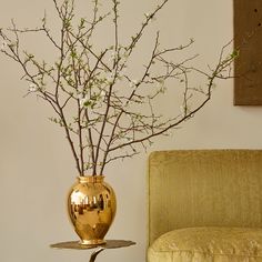 a gold vase with flowers in it sitting on a table next to a couch and chair