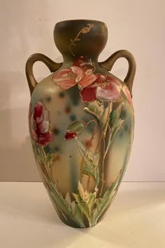 a vase with flowers painted on it sitting on a white table top next to a wall