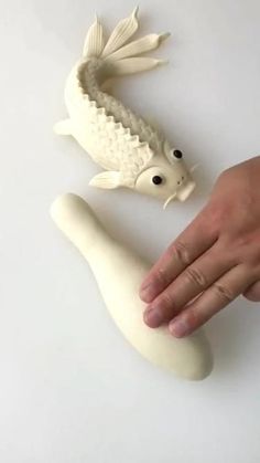 a hand is reaching for a fish on a white surface next to a fake foot