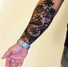 a man's arm with a palm tree and clock tattoo on his left arm