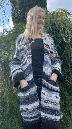 a woman standing in front of bushes wearing a blue and white striped cardigan sweater