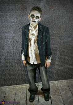 a young boy dressed up as a skeleton with makeup on his face and tie, standing in front of a wall