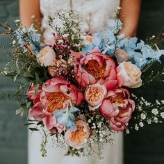 a bride holding a bouquet of pink and blue flowers on her wedding day in front of a brick wall