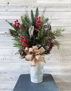 a vase filled with red berries and greenery on top of a blue table next to a wooden wall