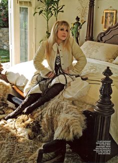 a woman sitting on top of a bed next to a sheepskin covered headboard