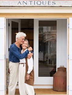 an older man and woman standing in the doorway of a store with their arms around each other