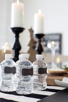 three bottled water bottles sitting on top of a black and white striped table cloth with candles in the background