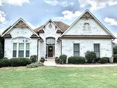 a large white brick house with green grass and bushes in front of it on a cloudy day