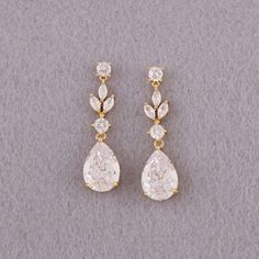 two pairs of gold and diamond earrings on a gray surface, one with a tear shaped drop