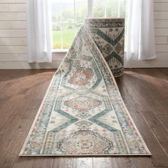 a rug on the floor in front of a window with white curtains and wooden floors