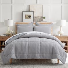 a bed with grey and white comforter in a bedroom next to two lamps on the nightstands