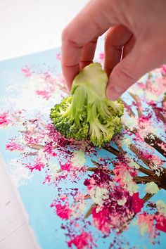 someone is peeling broccoli on a piece of blue paper with pink and white flowers