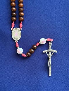 --- 1" St. Agatha/pink ribbon rosary center --- 1 7/8" Papal crucifix --- 10mm hand painted pink ribbon Our Father beads --- 8mm natural Madre de cacao wood Hail Mary beads --- stainless steel accent spacers --- pink micro cord  --- lightweight and approximately 17 inches long Please let us know, if you have any questions. Follow us on Instagram and Facebook @sistersinchristrosaries to see our latest designs. Please note that colors may differ slightly from how they appear on your screen due to varying monitor settings. Also, due to the nature of natural wood beads and gemstones, variety in wood grain pattern and coloration is to be expected. Handmade Pink Rosary With Cross Shape, Handmade Pink Rosary In Cross Shape, Handmade Pink Rosary With Cross, Adjustable Pink Cross Rosary, Handmade Pink Cross Rosary, St Agatha, Saint Agatha, Our Father, Hail Mary