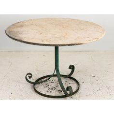 a marble top table with wrought iron base and circular design on the bottom, sitting on a white tile floor