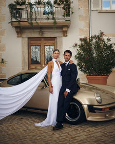 a man and woman standing next to a car with a white wedding dress on it