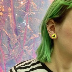 a woman with green hair wearing yellow earring and black and white striped shirt in front of colorful background