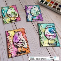 four cards with different designs on them sitting next to a paintbrush and watercolor palette