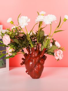 a vase filled with flowers next to a photo frame on a pink background and an image of a human heart