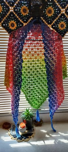 a rainbow colored umbrella hanging from the side of a window in front of a potted plant