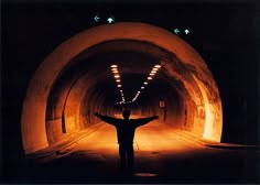 a man standing in the middle of a tunnel with his arms spread out and lights on