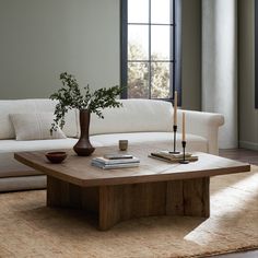 a living room with a couch, coffee table and vase on the floor in front of a window