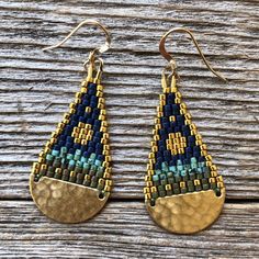 two pairs of gold and blue beaded earrings sitting on top of a wooden table