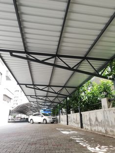 a white car parked under a covered parking lot next to a wall and tree's