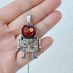 a hand holding a silver and red pendant with an image of a robot on it