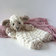 a stuffed sheep laying on top of a pink blanket