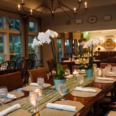 a dining room table with place settings and flowers in vases on the top tables